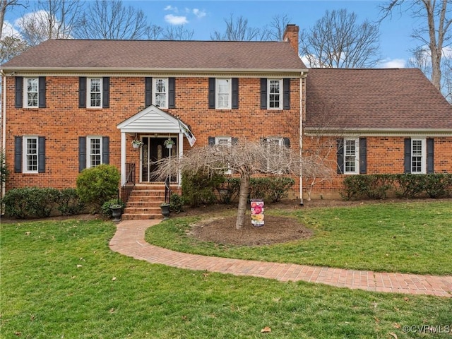 colonial house featuring a shingled roof, a chimney, a front lawn, and brick siding