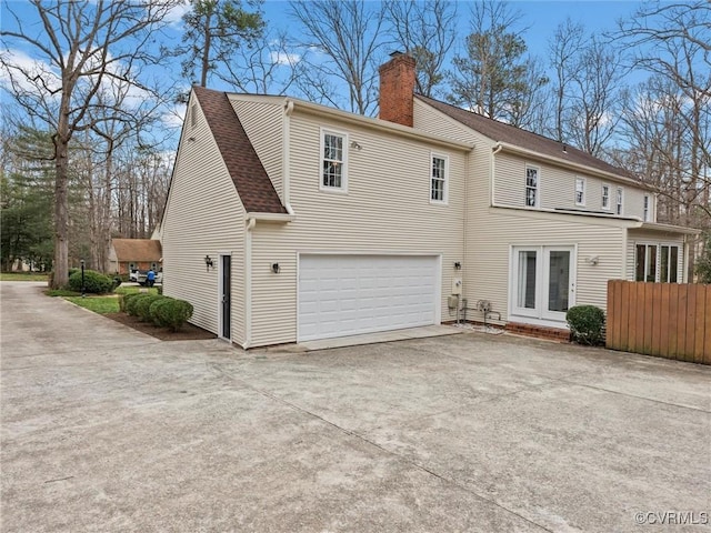 rear view of house featuring french doors, a chimney, a shingled roof, an attached garage, and driveway