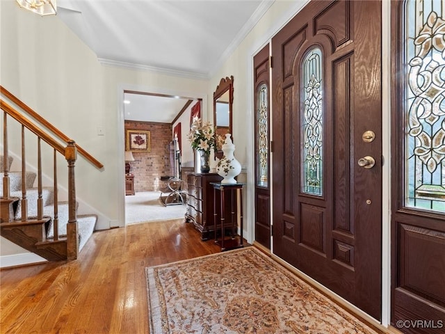 foyer featuring stairs, brick wall, ornamental molding, and wood finished floors