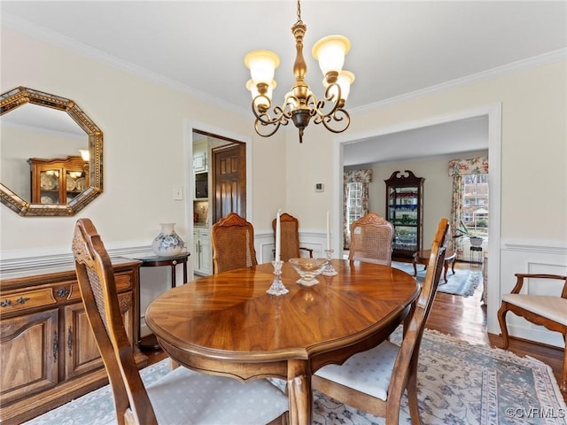 dining space with a decorative wall, wood finished floors, ornamental molding, wainscoting, and an inviting chandelier