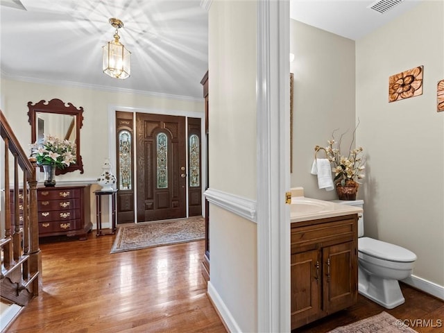 entryway with wood finished floors, visible vents, baseboards, stairs, and crown molding