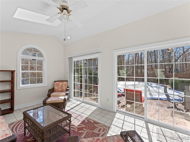 living area featuring vaulted ceiling with skylight, tile patterned flooring, baseboards, and a ceiling fan