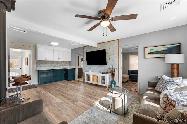 living room featuring light wood-style flooring, visible vents, baseboards, a ceiling fan, and beam ceiling