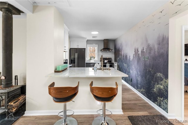 kitchen with appliances with stainless steel finishes, wood finished floors, a wood stove, wall chimney range hood, and a sink