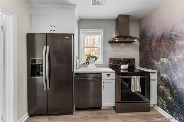 kitchen featuring visible vents, light wood-style flooring, stainless steel appliances, wall chimney range hood, and white cabinetry