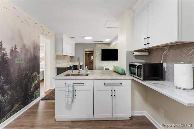 kitchen featuring a peninsula, wood finished floors, a sink, white cabinetry, and backsplash