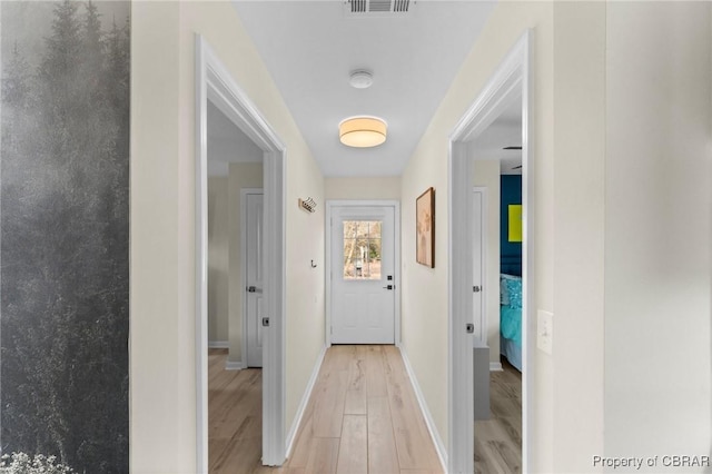 corridor with light wood-type flooring, visible vents, and baseboards