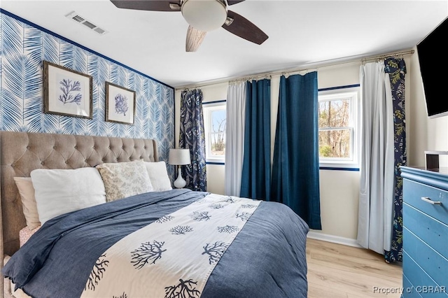 bedroom with visible vents, an accent wall, wood finished floors, baseboards, and wallpapered walls