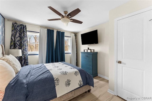 bedroom featuring baseboards, multiple windows, a ceiling fan, and light wood-style floors