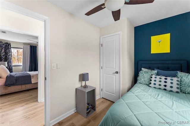 bedroom with light wood-style floors, visible vents, baseboards, and a ceiling fan