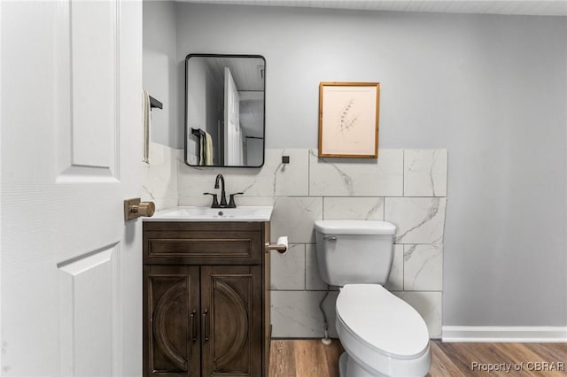 half bath with toilet, tile walls, wood finished floors, and vanity