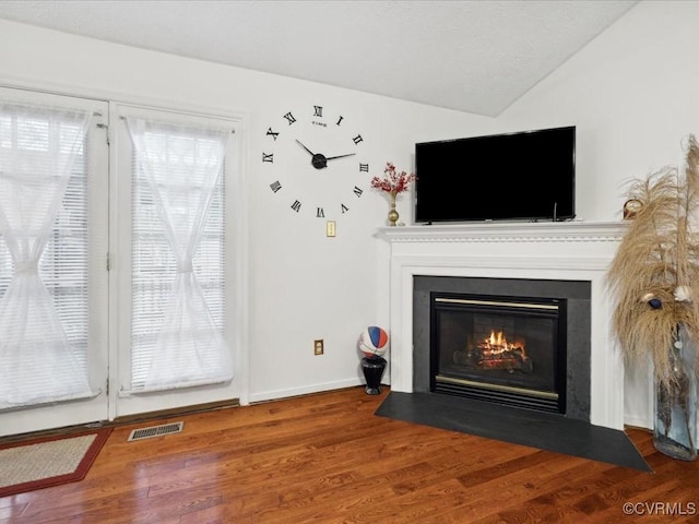 unfurnished living room with visible vents, a fireplace with flush hearth, vaulted ceiling, wood finished floors, and baseboards