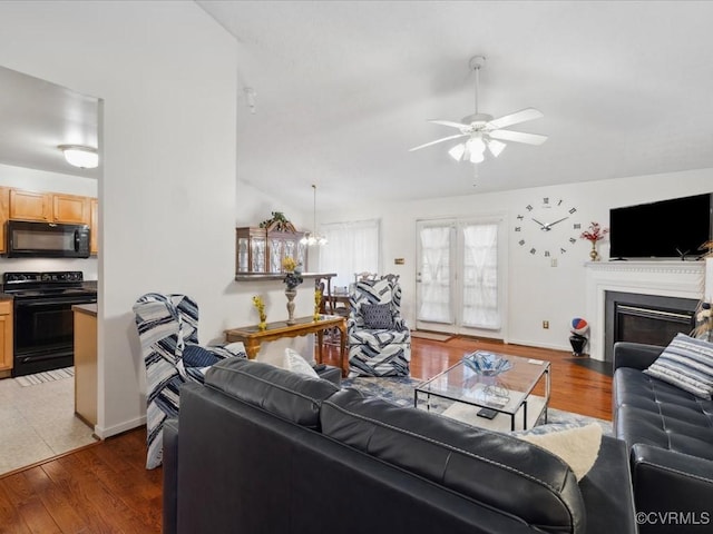 living room featuring baseboards, lofted ceiling, a fireplace with flush hearth, ceiling fan, and wood finished floors