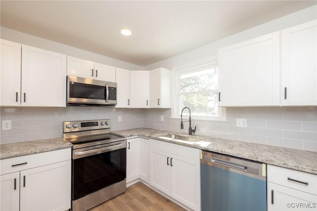 kitchen featuring a sink, light wood-style floors, white cabinets, appliances with stainless steel finishes, and tasteful backsplash