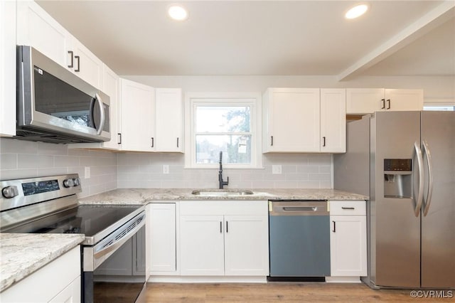 kitchen featuring appliances with stainless steel finishes, white cabinetry, a sink, and light stone counters