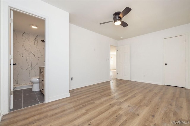 unfurnished bedroom featuring ensuite bathroom, wood finished floors, and baseboards