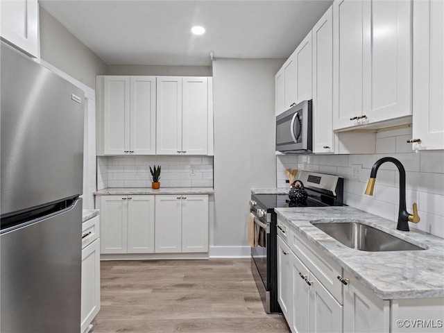 kitchen with a sink, stainless steel appliances, white cabinets, and light wood finished floors