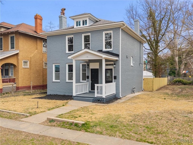 traditional style home featuring brick siding, a front lawn, fence, a porch, and a chimney