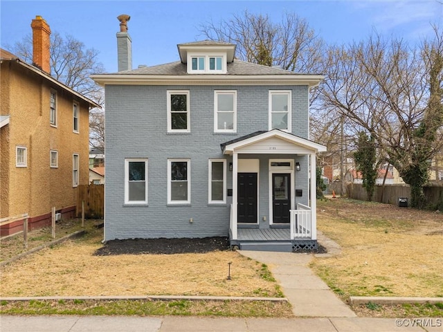 american foursquare style home featuring brick siding, a front lawn, fence, covered porch, and a chimney