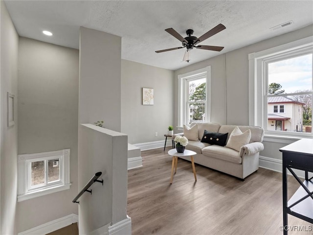 living area featuring ceiling fan, visible vents, baseboards, and light wood-style flooring