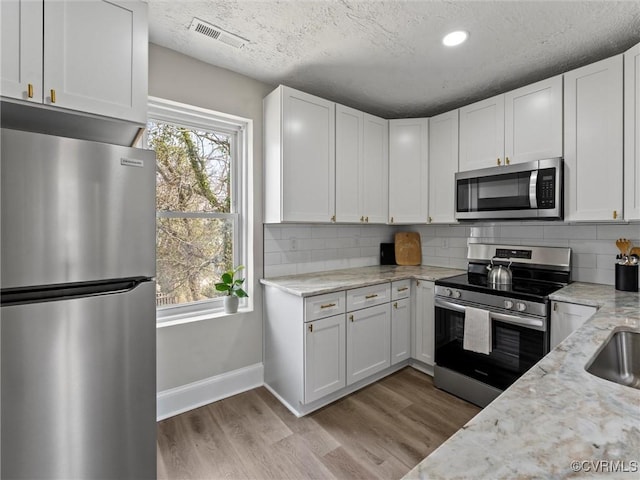 kitchen featuring decorative backsplash, light wood finished floors, visible vents, and appliances with stainless steel finishes