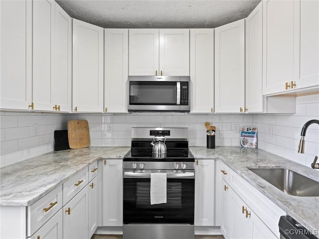 kitchen with a sink, stainless steel appliances, light stone countertops, and white cabinets