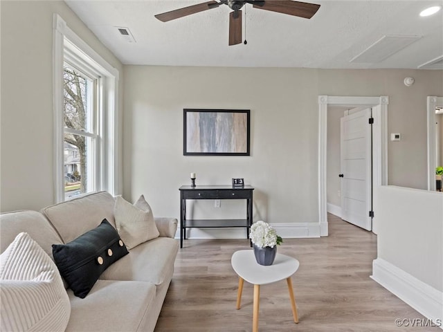 living room with a ceiling fan, visible vents, baseboards, light wood finished floors, and attic access