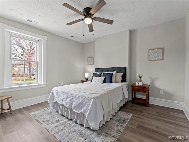 bedroom featuring a ceiling fan, wood finished floors, visible vents, baseboards, and a textured ceiling