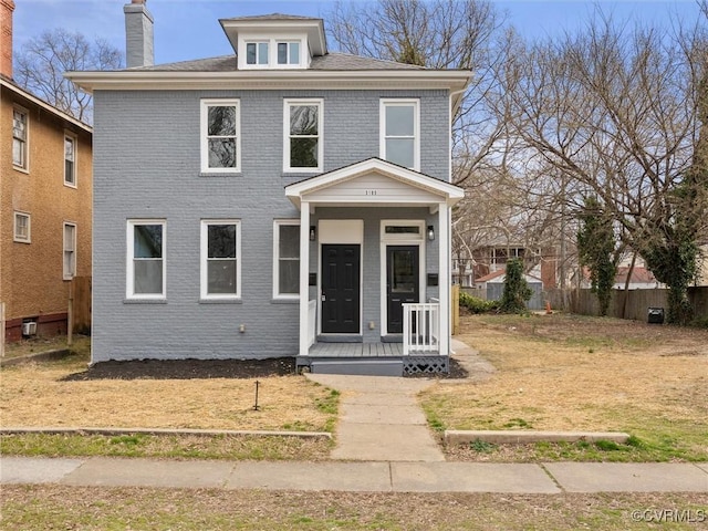 traditional style home featuring brick siding, covered porch, a chimney, and fence