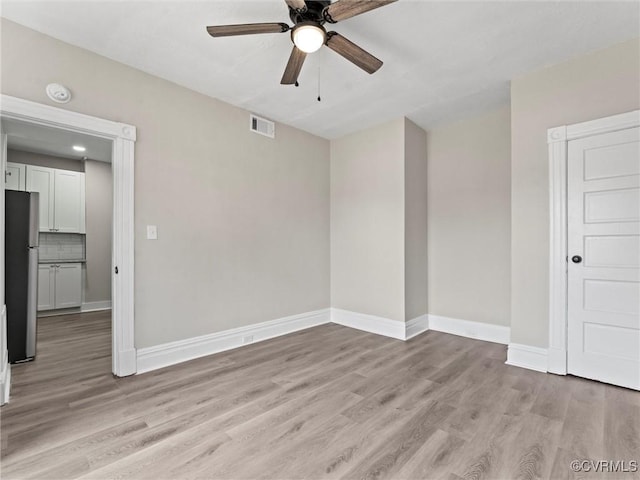 empty room featuring light wood-type flooring, baseboards, visible vents, and ceiling fan