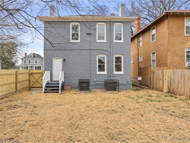 rear view of property with central AC unit, a chimney, and a fenced backyard