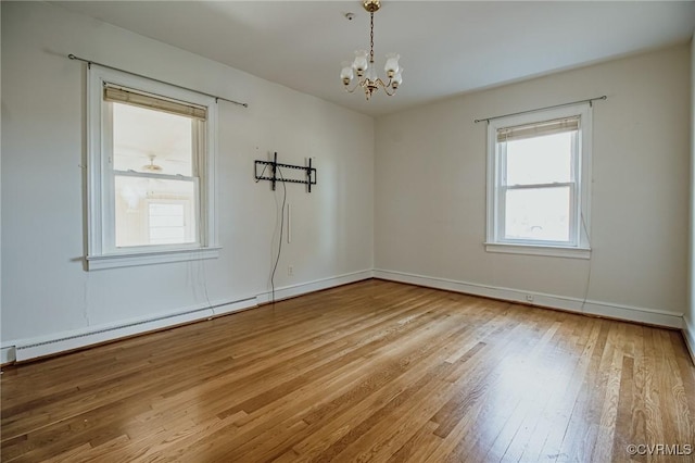 empty room with a notable chandelier, baseboards, baseboard heating, and hardwood / wood-style floors