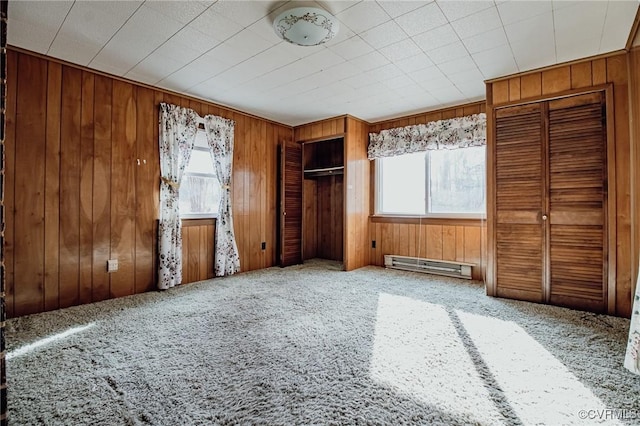 unfurnished bedroom with carpet floors, wood walls, a baseboard radiator, and multiple closets