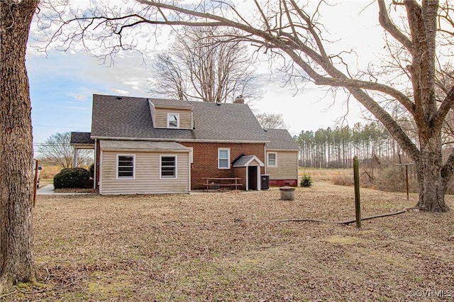 back of property featuring a shingled roof, a chimney, and brick siding