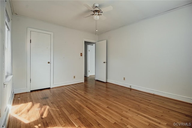 unfurnished bedroom with ceiling fan, a baseboard heating unit, wood finished floors, and baseboards