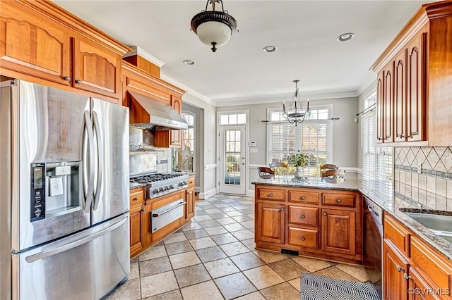 kitchen with a warming drawer, appliances with stainless steel finishes, a peninsula, brown cabinetry, and wall chimney range hood