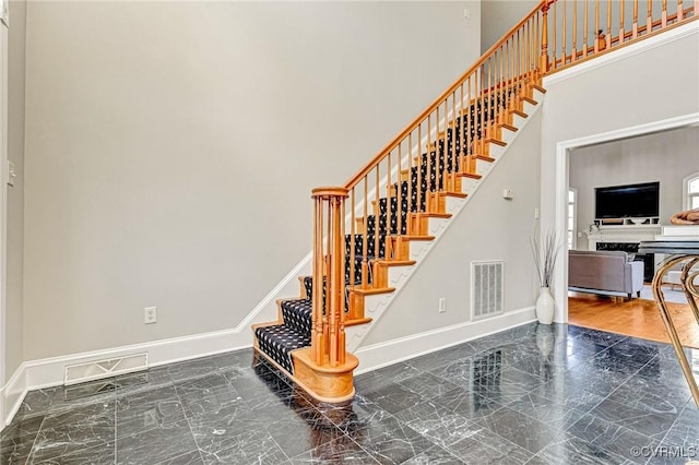 stairway featuring visible vents, marble finish floor, baseboards, and a towering ceiling