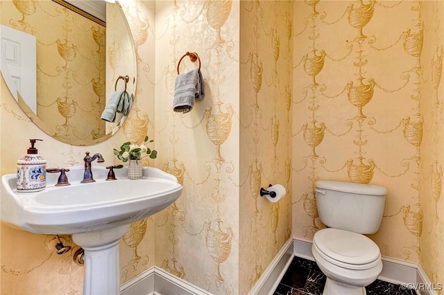 half bathroom with marble finish floor, toilet, and baseboards