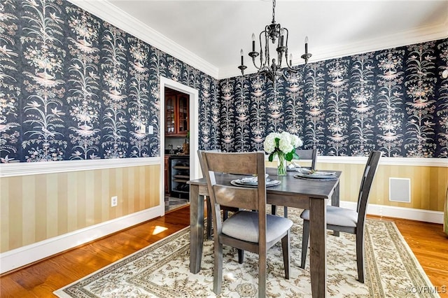 dining room with a wainscoted wall, wallpapered walls, crown molding, and wood finished floors