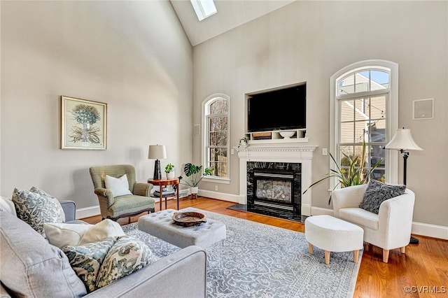 living room featuring wood finished floors, baseboards, high vaulted ceiling, a skylight, and a high end fireplace