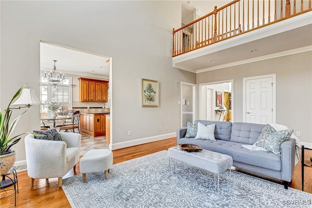 living area featuring baseboards, a towering ceiling, crown molding, a notable chandelier, and light wood-type flooring