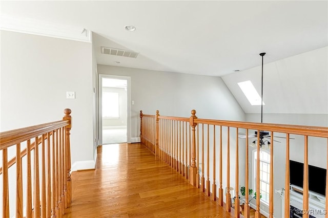 hall with visible vents, baseboards, an upstairs landing, vaulted ceiling with skylight, and wood finished floors