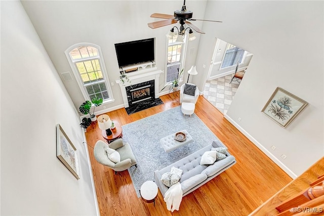 living area with ceiling fan, a premium fireplace, baseboards, and wood finished floors