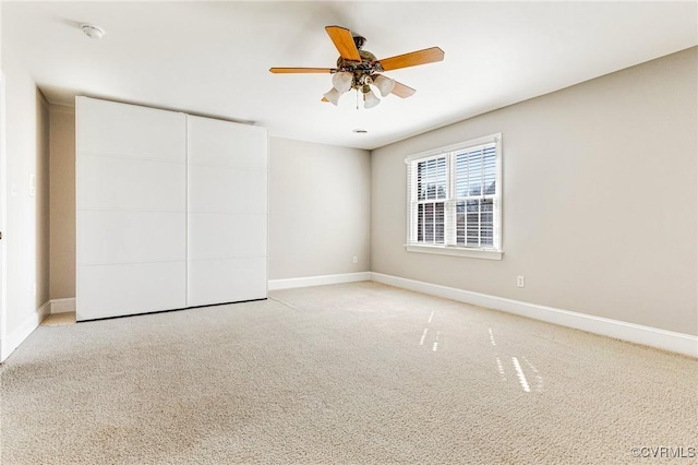 spare room with light colored carpet, a ceiling fan, and baseboards