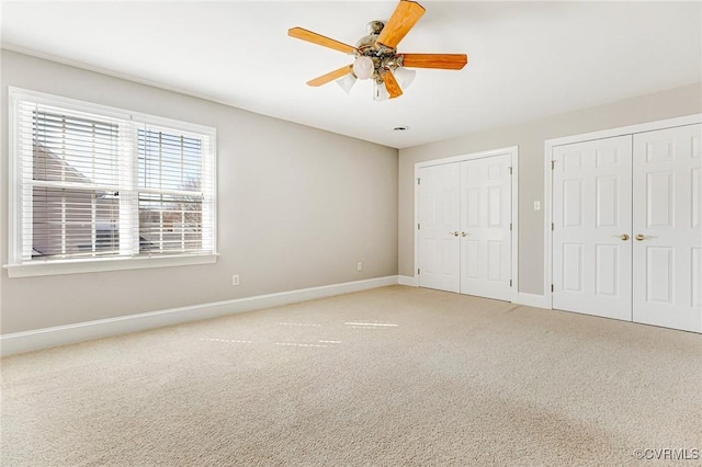 unfurnished bedroom featuring carpet flooring, baseboards, multiple closets, and ceiling fan