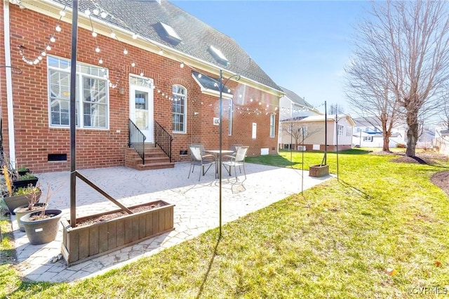 rear view of house featuring a lawn, a patio, a shingled roof, crawl space, and brick siding