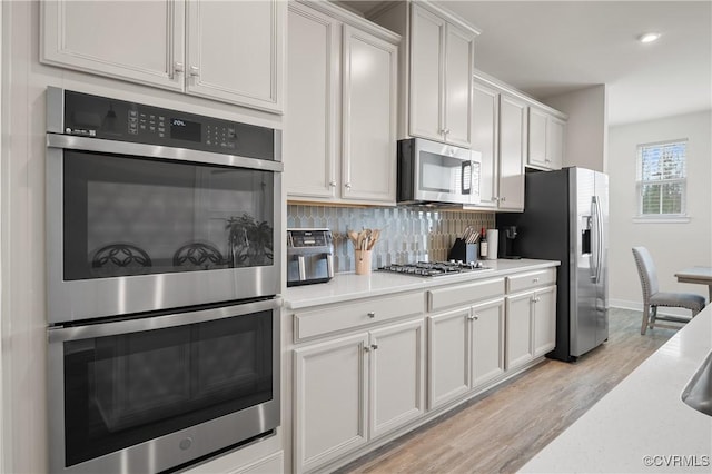 kitchen with light wood-style flooring, stainless steel appliances, decorative backsplash, and light countertops