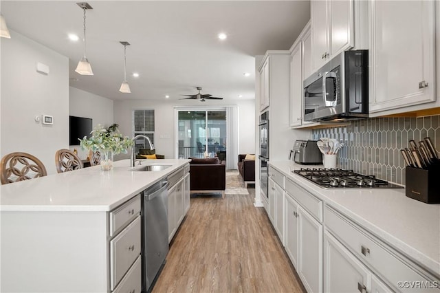 kitchen with stainless steel appliances, a sink, open floor plan, light countertops, and tasteful backsplash