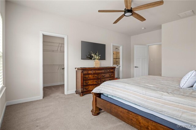 bedroom featuring light carpet, baseboards, ceiling fan, a walk in closet, and a closet