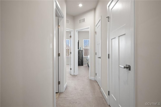 corridor with light carpet, visible vents, and baseboards